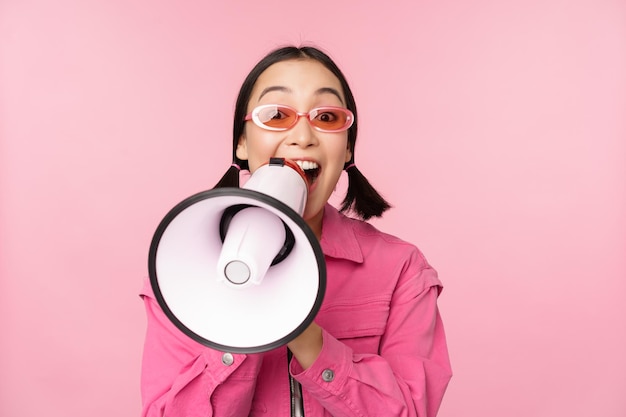 注目の発表コンセプトピンクの背景の上に立っているスピーカー募集でメガホン広告で叫んでいる熱狂的なアジアの女の子