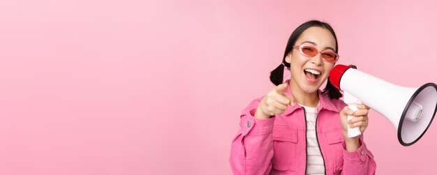 Attention announcement concept Enthusiastic asian girl shouting in megaphone advertising with speaker recruiting standing over pink background