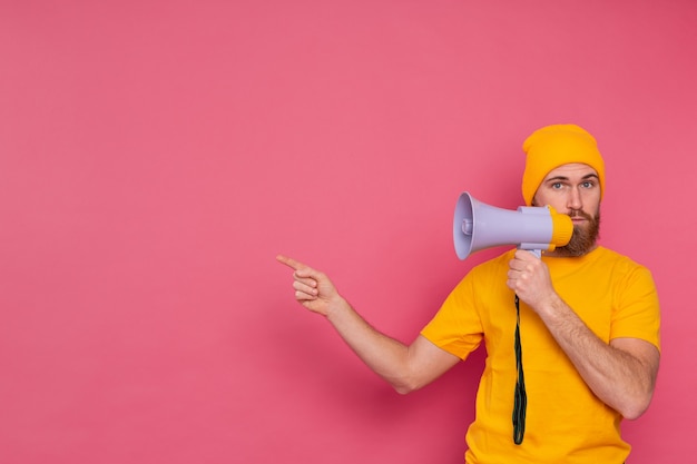 Attention! European man with megaphone pointing finger to the left on pink background