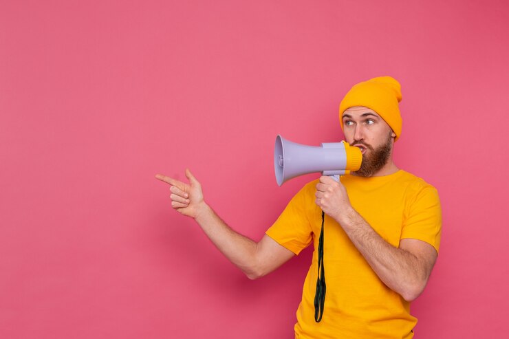 Free Photo attention! european man with megaphone pointing finger to the left on pink background