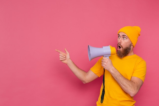 Attention! European man with megaphone pointing finger to the left on pink background