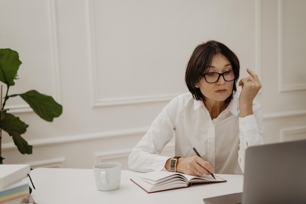 Foto gratuita un'attenta signora bruna caucasica adulta con gli occhiali si siede sul posto di lavoro dell'ufficio concetto di ework