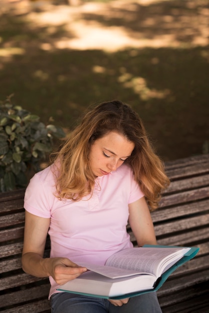 Бесплатное фото Внимательный подросток женщина читает учебник на скамейке
