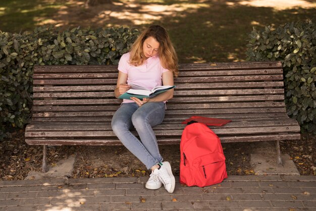 Внимательная подростковая женщина с учебником на скамейке