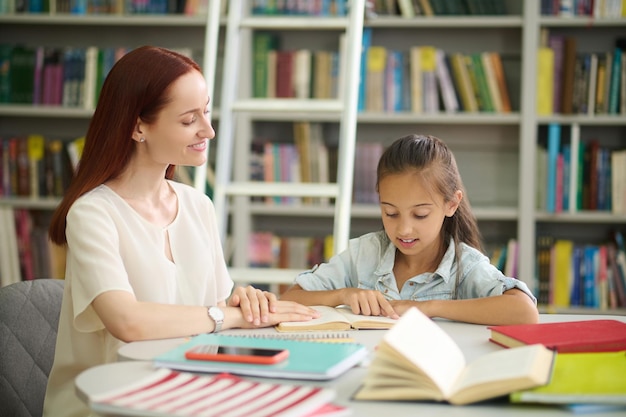 Free photo attentive woman listening to girl reading diligently