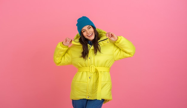 Free photo attractive active woman model posing on pink wall in colorful winter down jacket of bright yellow color, warm coat fashion trend