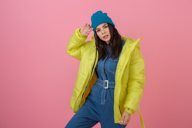 Attractive active woman model posing on pink wall in colorful winter down jacket of bright yellow color, warm coat fashion trend