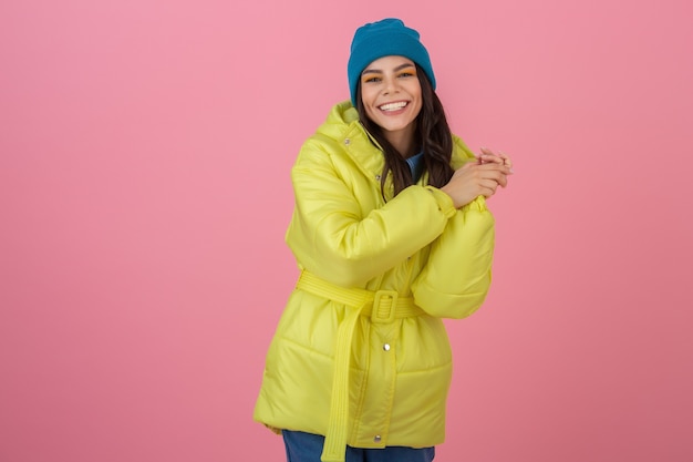 Attractive active woman posing on pink wall in colorful winter down jacket of bright yellow color, smiling fun, warm coat fashion trend, crazy shocked surprised face expression