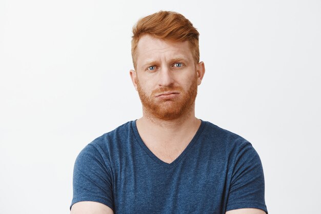 attractive adult caucasian redhead guy with bristle, pursing lips and frowning being troubled to answer, stuck in tough and annoying situation, breathing out, feeling questioned