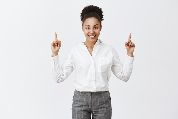 Attractive african-american female entrepreneur pointing fingers up and smiling