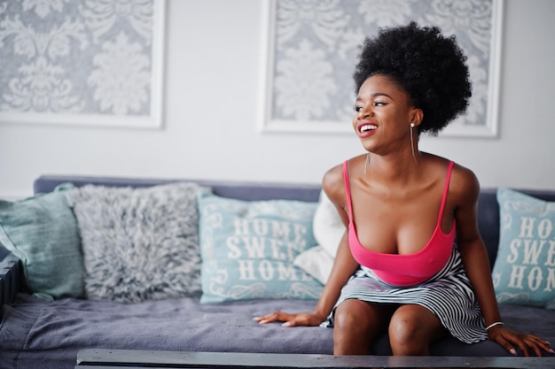 Attractive african american woman with afro hair wear on skirt pink top posed at white room Fashionable sexy black model