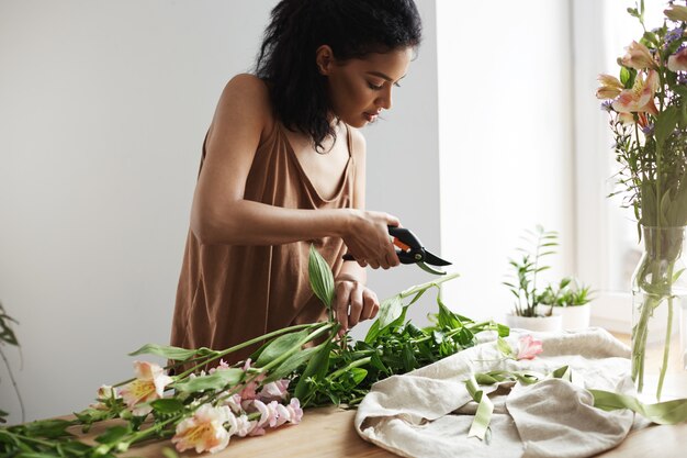 Attractive african female florist cutting flower stems at workplace.