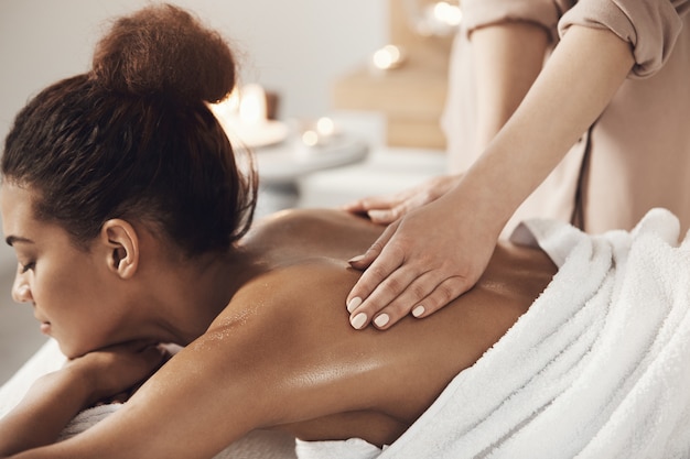 Free photo attractive african woman having massage relaxing in spa salon. closed eyes.