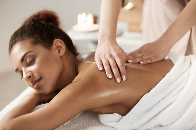 Free photo attractive african woman having massage relaxing in spa salon. closed eyes.