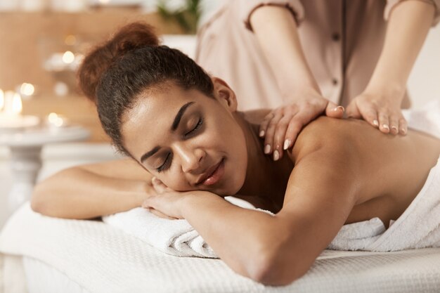 Attractive african woman having massage relaxing in spa salon. Closed eyes.