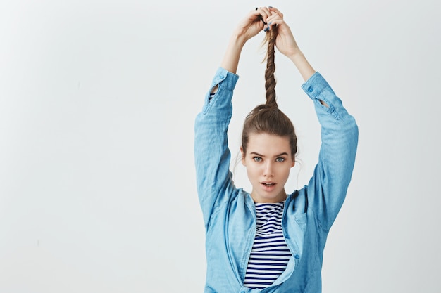 Free photo attractive ambitious confident young woman pulling twisting hair up looking daring sexy camera, wearing trendy loose clothes, satisfied result applying new shampoo haircare,