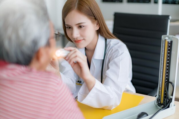 매력적인 아시아 의사 여성이 병원에서 노인 아시아 환자의 혀 목구멍 시스템을 확인합니다.