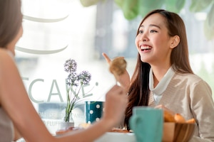 Attractive asian female talking good positive conversation to friends with smiling laugh and happiness moment at counter near window at cafe with daylight from garden positive attitude relationship