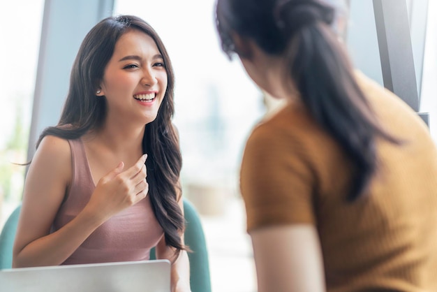 Attractive asian positive female happiness conversation smiling laugh cheeful talking with friend at cafe restaurant with natural light from window casual lifestyle concept