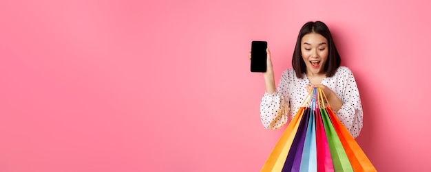 무료 사진 애플리케이션 standi를 통해 온라인으로 구매하는 스마트폰 앱과 쇼핑백을 보여주는 매력적인 아시아 여성