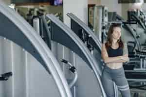 Бесплатное фото Привлекательная спортивная девушка стоит на стене тренажеров в тренажерном зале. здоровый образ жизни.