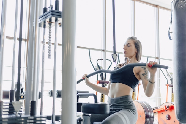 Привлекательная спортивная девушка тренирует плечи в симуляторе. вид мышц спины. здоровый образ жизни.