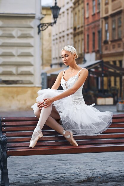 Привлекательная балерина сидит на скамейке в городе