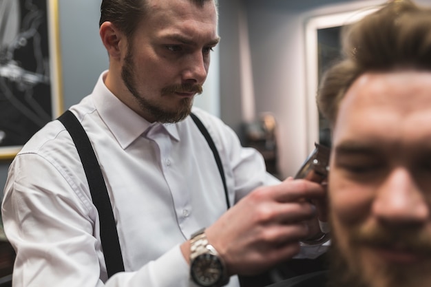 Attractive barber shaving hair of client