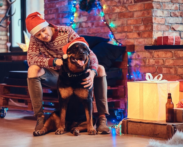 クリスマスの装飾が施された部屋で彼のロットワイラー犬と魅力的なひげを生やしたヒップスターの男性。