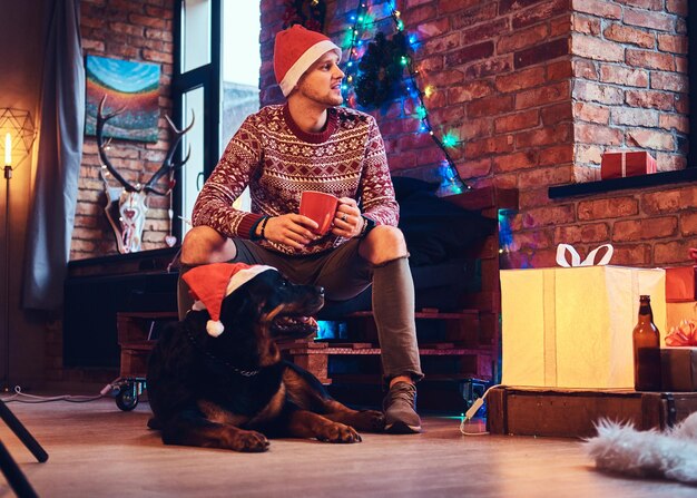Attractive bearded hipster male with his Rottweiler dog in a room with Christmas decoration.