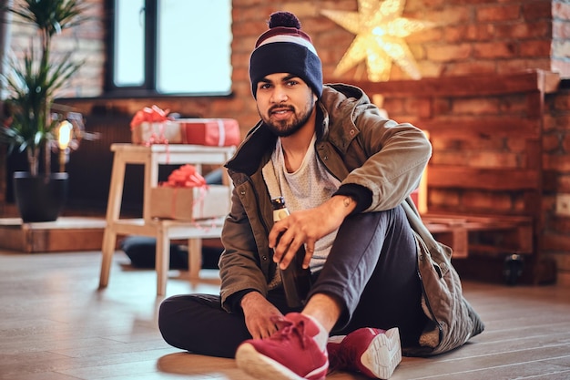 Attractive bearded Indian male drinks craft beer in a room with Christmas decoration.