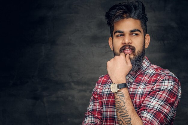 Attractive bearded Indian man in plaid fleece shirt over grey background.