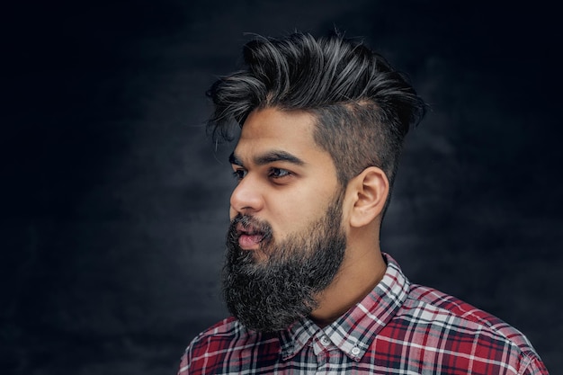 Attractive bearded Indian man in plaid fleece shirt over grey background.
