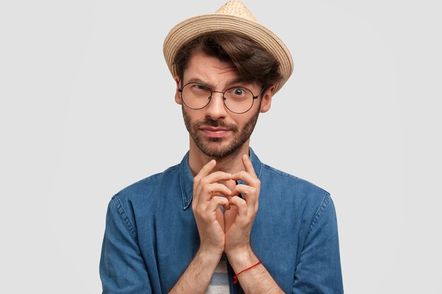 Attractive bearded male keeps hands together and looks with intriguing look