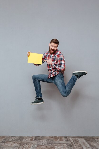 Attractive bearded man holding blank paper and jumping