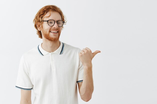 Attractive bearded redhead guy posing against the white wall with glasses