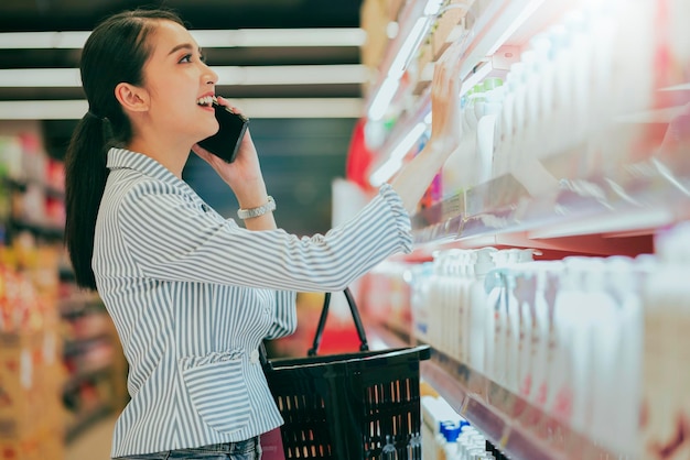 Attractive beautiful asian young woman shopping for diary products at a grocery storesupermarket Shopping In Supermarket Groceries Store Standing In Aisle With Shop Trolley Buyer Choosing product