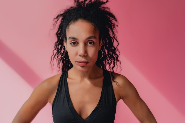 Attractive black african american woman in black leggins fitness outfit on pink background