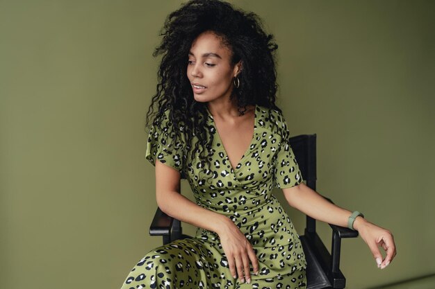 Attractive black african american woman posing in stylish green dress isolated on green background