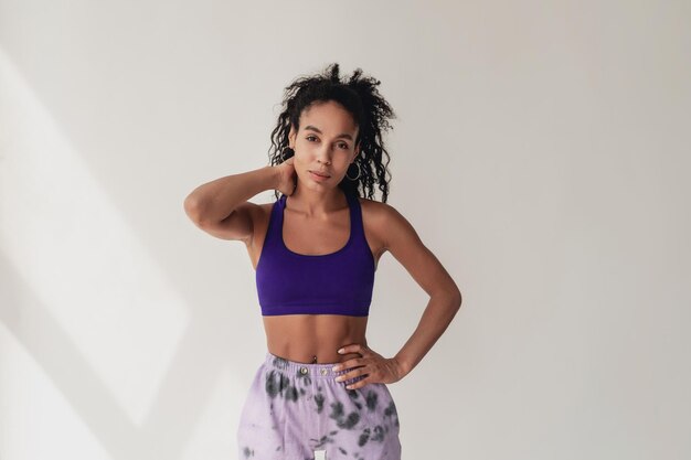 Attractive black african american woman in stylish hipster fitness outfit violet top and pants on white isolated background summer fashion trend happy smiling curly hair sport style