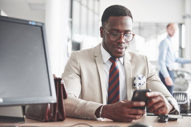 Attractive black businessman sits at the table at the car dealership, he signs a contract and buys a new car.