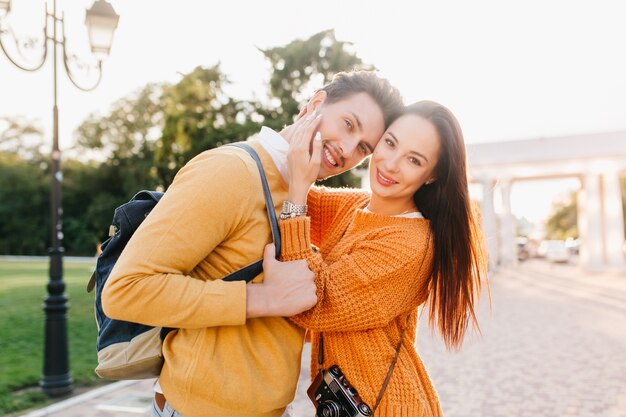 Attractive black-haired woman with elegant manicure gently touching boyfriend's face and smiling in park