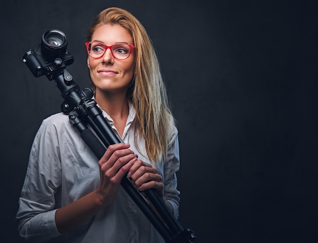 An attractive blond female photographer taking pictures with professional camera on a tripod.