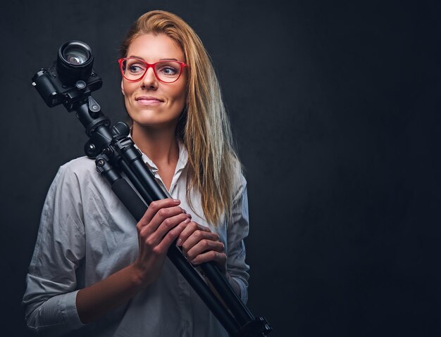 An attractive blond female photographer taking pictures with professional camera on a tripod.