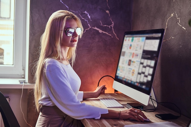 Free photo attractive blond girl is studying at her modern room using computer.