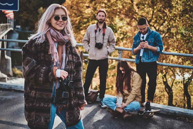 Привлекательная блондинка с фотоаппаратом наслаждается осенней прогулкой со своими друзьями.