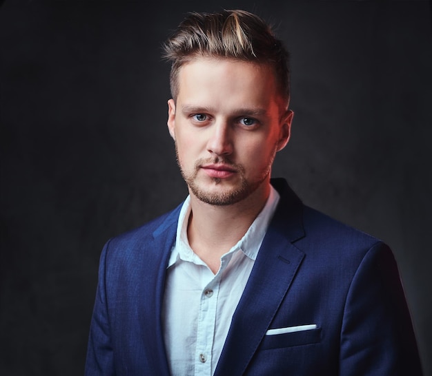 Free photo an attractive blond male dressed in a suit over dark grey background.