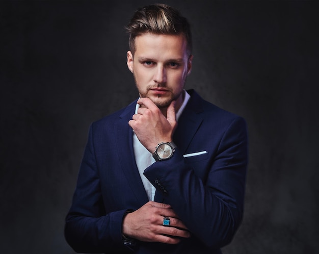 An attractive blond male dressed in a suit over dark grey background.