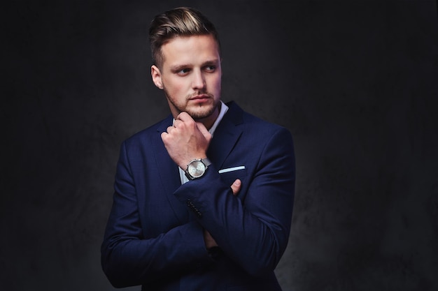 An attractive blond male dressed in a suit over dark grey background.