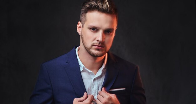 An attractive blond male dressed in a suit over dark grey background.